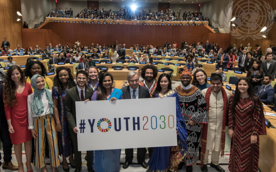 Photo of young people standing with the secretary general holding up a sign saying #Youth2030